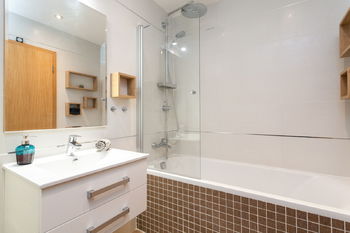 Koupelna s vanou a skleněnou sprchovou zástěnou - Prodej bytu 2+kk v osobním vlastnictví 63 m², Praha 8 - Libeň