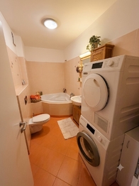 Koupelna bytu s vanou, WX, umyvadlem, topným žebříkem a prostotrem pro pračku i sušičku. - Prodej bytu 2+kk v osobním vlastnictví 61 m², Praha 9 - Letňany
